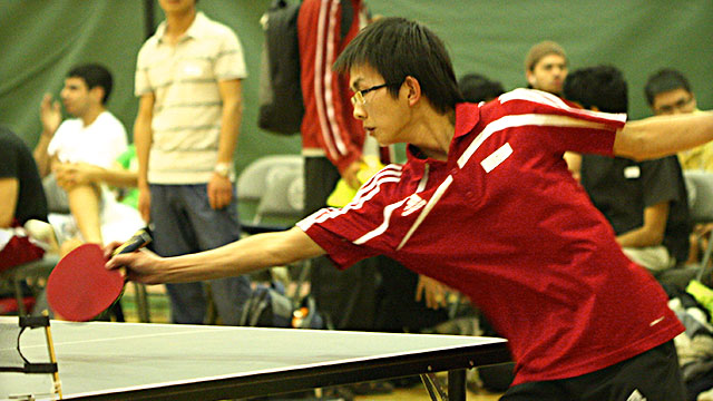A player reaches with a paddle during a table tennis match. 