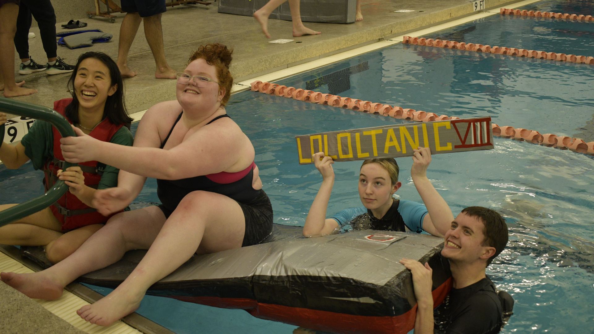 A team gathers on and around a cardboard boat in the Activity Center Natatorium. 