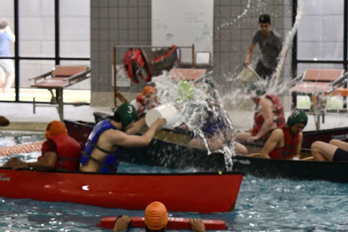 Students in canoes splash buckets of water on each other in the Activity Center Natatorium.  